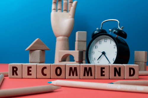 Recommend spelled out in blocks with wooden hand raised, blocks, and alarm clock in the background