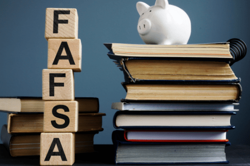 Stacked wooden blocks that read FAFSA and a piggy bank on top of books
